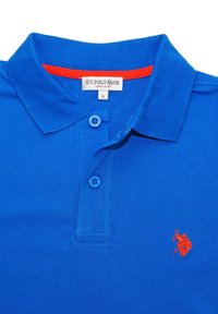 Polo en coton bleu avec une patte de boutonnage à trois boutons, présentant un logo orange brodé sur le côté gauche de la poitrine et un détail de col contrastant.