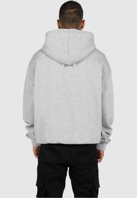 Sweatshirt gri cu glugă, design oversized, material texturat, șnur la glugă, manșete și tiv ribbate, purtat cu pantaloni cargo negri.