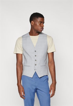 Gilet à carreaux gris avec cinq boutons, deux poches, porté sur un t-shirt beige clair. Assorti à un pantalon bleu, avec une coupe élégante.