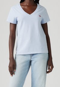 Světle modré bavlněné tričko s V-výstřihem, krátkými rukávy a malým červeným logem na levé stran�ě hrudi. Hladká textura s volným střihem.