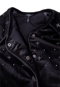 Giacca di velluto nero con cuciture decorative in argento, bottoni a scatto e una consistenza morbida. La fodera interna è liscia con una tonalità grigia.