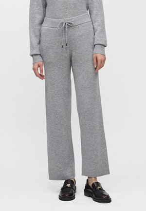 Personne portant un pantalon large en maille gris clair avec une taille à cordon, associé à des mocassins en cuir noir.