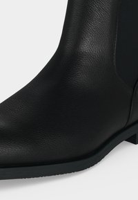 Gros plan sur l'avant et le côté d'une bottine en cuir noir avec un petit talon et une surface texturée.