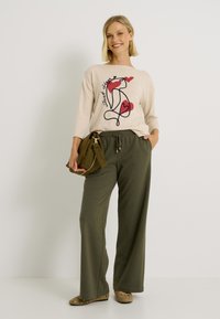 Pull beige avec un imprimé graphique de cœurs rouges ; associé à un pantalon ample vert olive et un sac à épaule vert.
