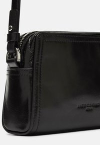 Schwarze Lederhandtasche mit glatter, glänzender Textur, ausgestattet mit einem Reißverschluss und einem verstellbaren Tragegurt. Dezente geprägte Logodetails.