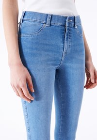 Jeans de mezclilla de color azul claro con un diseño ajustado, estilo de cinco bolsillos y una textura suave. Con cierre de cremallera y presillas para el cinturón en la cintura.