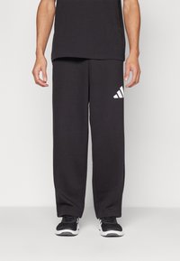 Sorte atletiske sweatpants lavet af blødt stof, med en løs pasform, elastisk talje og et hvidt Adidas-logo på venstre lår.