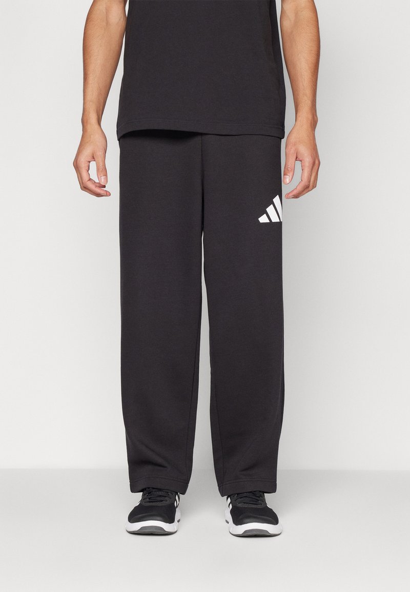 Sorte atletiske sweatpants lavet af blødt stof, med en løs pasform, elastisk talje og et hvidt Adidas-logo på venstre lår.
