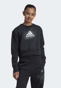 Sudadera negra y pantalones con el logotipo blanco de Adidas y un patrón de puntos dispersos. El material parece suave; diseño recortado con puños acanalados.