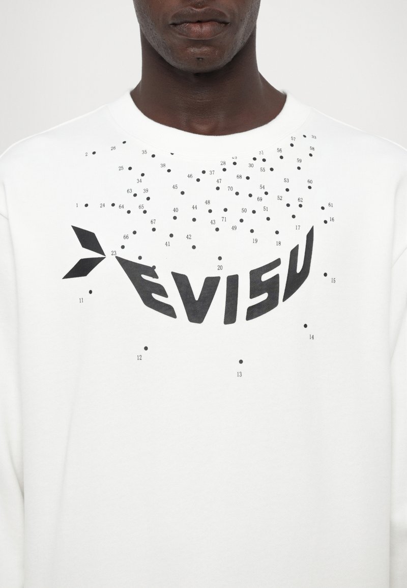 Vit sweatshirt med en stor svart "EVISU"-logotyp och spridda svarta prickar, med rundad halsringning och mjuk textur.