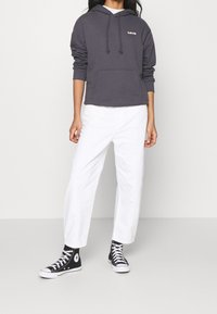 Felpa con cappuccio grigio scuro con tasca frontale e logo "Levi's" rosa, abbinata a pantaloni bianchi e sneakers nere alte.