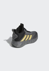 Black and gray athletic shoe with a flexible mesh upper, yellow accent stripes, and a textured sole for grip. Features a pull tab on the heel.