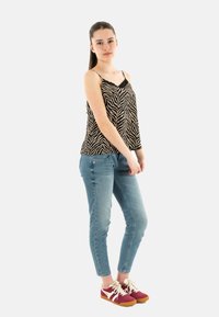Camiseta sin mangas de estampado de cebra en negro y beige con ribetes de encaje, combinada con jeans ajustados azul claro y zapatillas burdeos con detalles en beige.