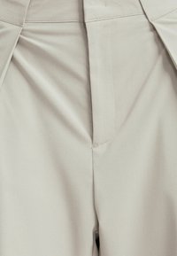 Tessuto beige e texturizzato con un design su misura, caratterizzato da pieghe frontali e cuciture pulite lungo la vita e i lati.