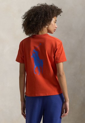 Κόκκινη βαμβακερή κοντομάνικη μπλούζα με στρογγυλή λαιμόκοψη. Διαθέτει μπλε γραφικό παίκτη πόλο στην πλάτη. Ισιόκοπη με κοντά μανίκια.