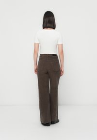 Bruine corduroy wijde broek met twee achterzakken en riemlussen, gecombineerd met een slim-fit witte top met korte mouwen.
