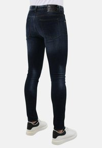 Donkerblauwe skinny jeans met een gladde denimtextuur, voorzien van achterzakken, subtiele stiksels en een zwart leren merklabel op de tailleband.