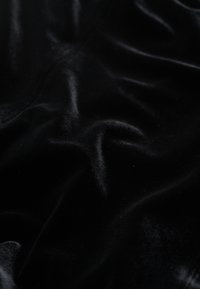 Zwarte fluwelen stof met een gladde, zachte textuur, met subtiele golven en kreukjes die de diepte en visuele aantrekkingskracht versterken.