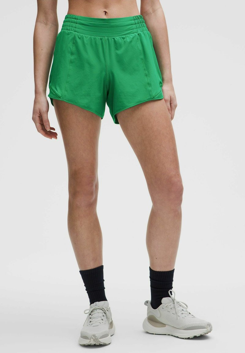 Pantalones cortos deportivos verdes con una cinturilla alta y fruncida y bolsillos laterales inclinados. Tejido suave, de longitud por encima de la rodilla, diseñado para ropa activa.