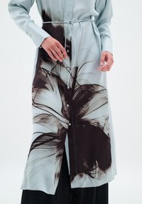 Rochie cambrată de culoare albastru deschis, cu un model floral alb-negru, închidere cu nasturi și un șnur în talie. Textură de țesătură netedă.