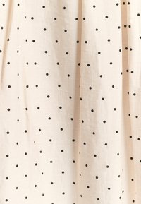 Cream fabric with evenly spaced small black polka dots and natural folds creating texture and depth across the surface.
