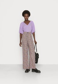 Top texturizado em lavanda com mangas volumosas combinado com calças largas de cintura alta, florais em roxo, amarelo e preto. Sapatos de plataforma pretos.