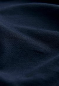 Tamsiai mėlynas medvilnės audinys su lygia tekstūra, rodantis subtilias bangas ir raukšles. Nėra matomų raštų ar puošmenų.