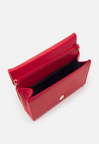 Punainen keinonahkainen lompakko, jossa on kultainen nappisulku, musta sisustus ja vetoketjullinen osasto, jossa on siistit linjat ja rakenteellinen muotoilu.
