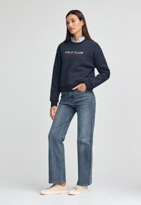 Sudadera azul marino con el logo "POLO CLUB", combinada con jeans de mezclilla azul claro y zapatillas beige. Presenta cuello redondo y puños acanalados.