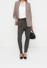 Brązowo-biała kratowana marynarka, biała koronkowa bluzka, oliwkowe spodnie, czarna torebka i czarne szpilki. Kluczowe cechy to faktury i dopasowanie.