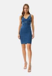 Denim bodycon dress with wide straps, V-neckline, metal hardware detail at the waist, and a fitted silhouette. Rich blue color, smooth texture.