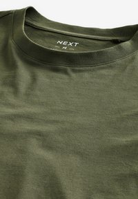 Olivgrünes Baumwoll-T-Shirt mit Rundhalsausschnitt, ausgestattet mit einer weichen Textur und dezentem Stretch. Das Etikett trägt die Aufschrift "NEXT" in Weiß.
