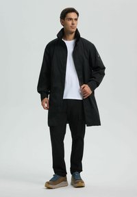 Cazadora negra de manga larga con cuello alto, fabricada en material ligero, que presenta un cierre frontal de botones y un detalle sutil del logo en las mangas.