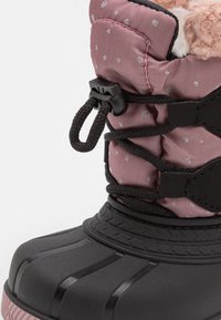 Zwarte waterdichte laars met een gestructureerde rubberen zool en een roze nylon bovenkant met zilveren stippen, verstelbare veters en een zachte voering van bont.