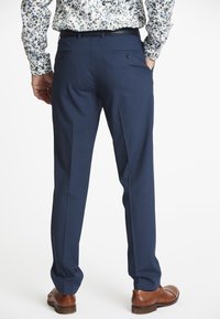 Marineblaue maßgeschneiderte Hose mit flachem Vorderteil, zwei Gesäßtaschen und glatter Textur, kombiniert mit braunen Lederschuhen.