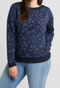 Sudadera azul marino con estampado floral en un tono azul más claro. Presenta un cuello redondo y puños y dobladillo acanalados. Tejido suave, corte relajado.