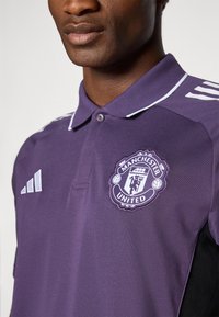 Lilla polo t-shirt med Manchester United-logo på brystet, med hvide detaljer på kraven og skuldrene, lavet af åndbart stof.