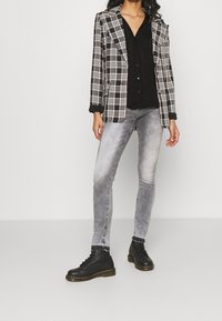 Blazer a quadri in bianco e nero, camicia nera, jeans grigi chiari slim-fit e stivali neri con lacci e suola gialla.