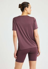 Top sportivo color marsala realizzato in tessuto morbido, maniche corte e vestibilità rilassata, abbinato a pantaloni corti color marsala.
