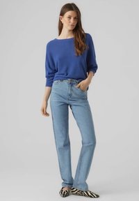 Modra pletena pulover z širokim izrezom, v kombinaciji s svetlo modrimi ravnimi jeans hlačami in črnobrnimi balerinkami s tiskanjem zebra.