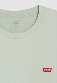 Světle zelené bavlněné tričko s kulatým výstřihem a malým červeným logem Levi's vyšitým na hrudi. Textura látky je hladká a jednolitá.