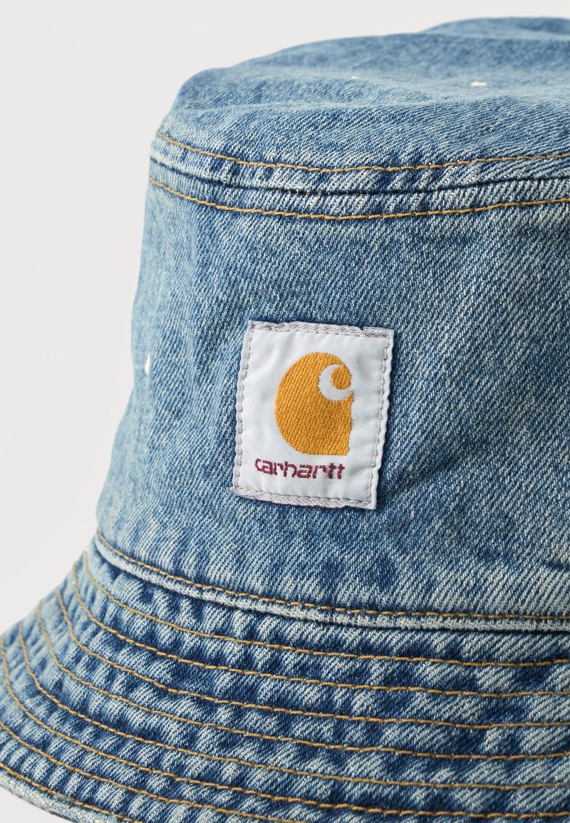 Denim bucket hat met Carhartt-logo patch met gele maansikkel en rode tekst aan de voorkant.