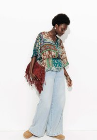 Blouse multicolore à motifs avec un décolleté en V, associée à un jean bleu clair à jambes larges et un sac à main bordeaux avec des franges.