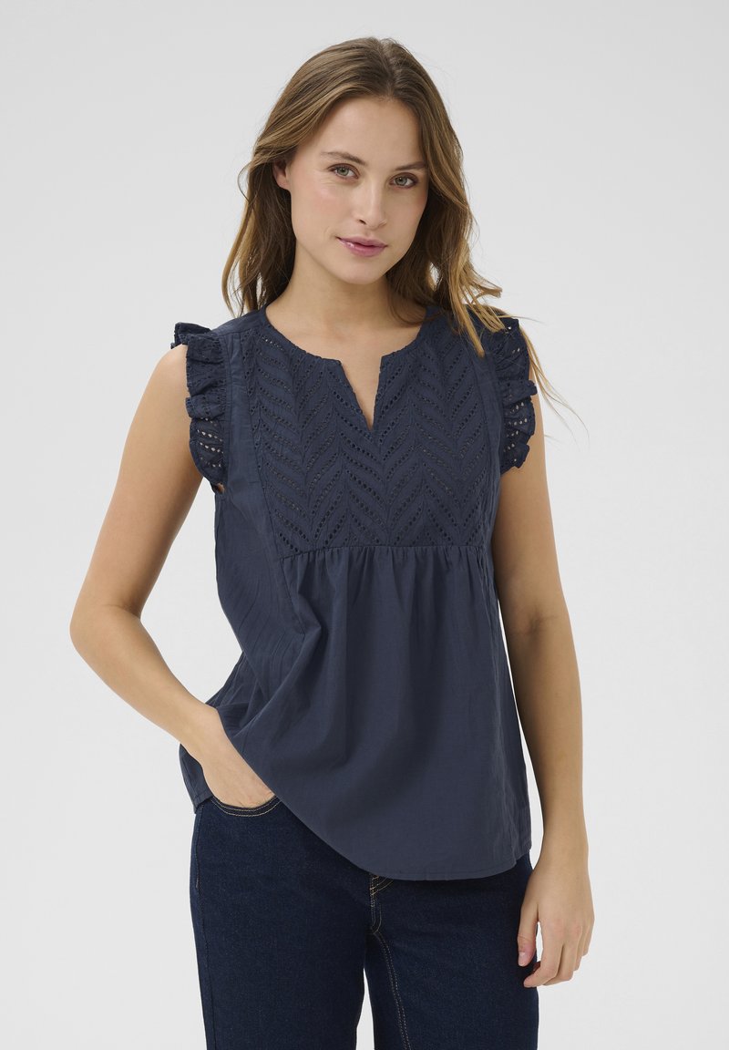 Blouse en coton bleu marine avec des manches courtes à volants et un décolleté en V profond. Présente une broderie détaillée avec un motif en chevron à l'avant.