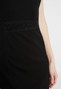 Mustapuku, jossa on teksturoitu kangas, tiukka muotoilu ja reunus, jossa on helminepristolut.