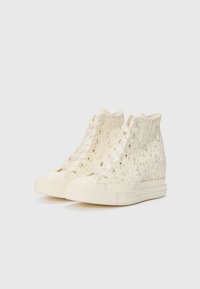 Höye sneakers i kremfarget lidding med et teksturert blomstermønster, med flate lisser og en gummitåhette, satt på en hvit plattformsåle.
