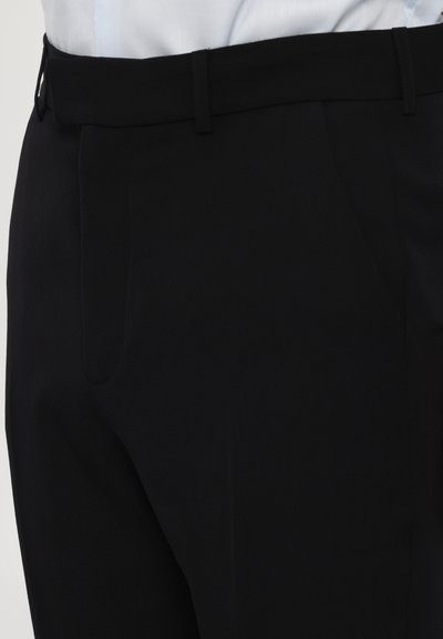 Pantalon noir avec une texture lisse, de coupe ajustée, doté de passants de ceinture et de poches latérales. Design sur mesure adapté aux environnements formels.