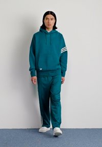 Completo tuta in teal con felpa con cappuccio e pantaloni affusolati. Presenta righe bianche sulle maniche e logo del marchio sul davanti. Tessuto morbido.