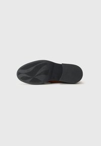 Semelle de chaussure en caoutchouc noir avec un motif ondulé texturé et des accents lisses. Forme arrondie et talon rectangulaire, avec un petit logo.