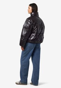 Juoda pūsta striukė su aukštu apykakliu, blizgia tekstūra, siuvinėta dygsniuoto dizaino ir laisvo silueto, derinama su džinsais ir laisvalaikio batais.